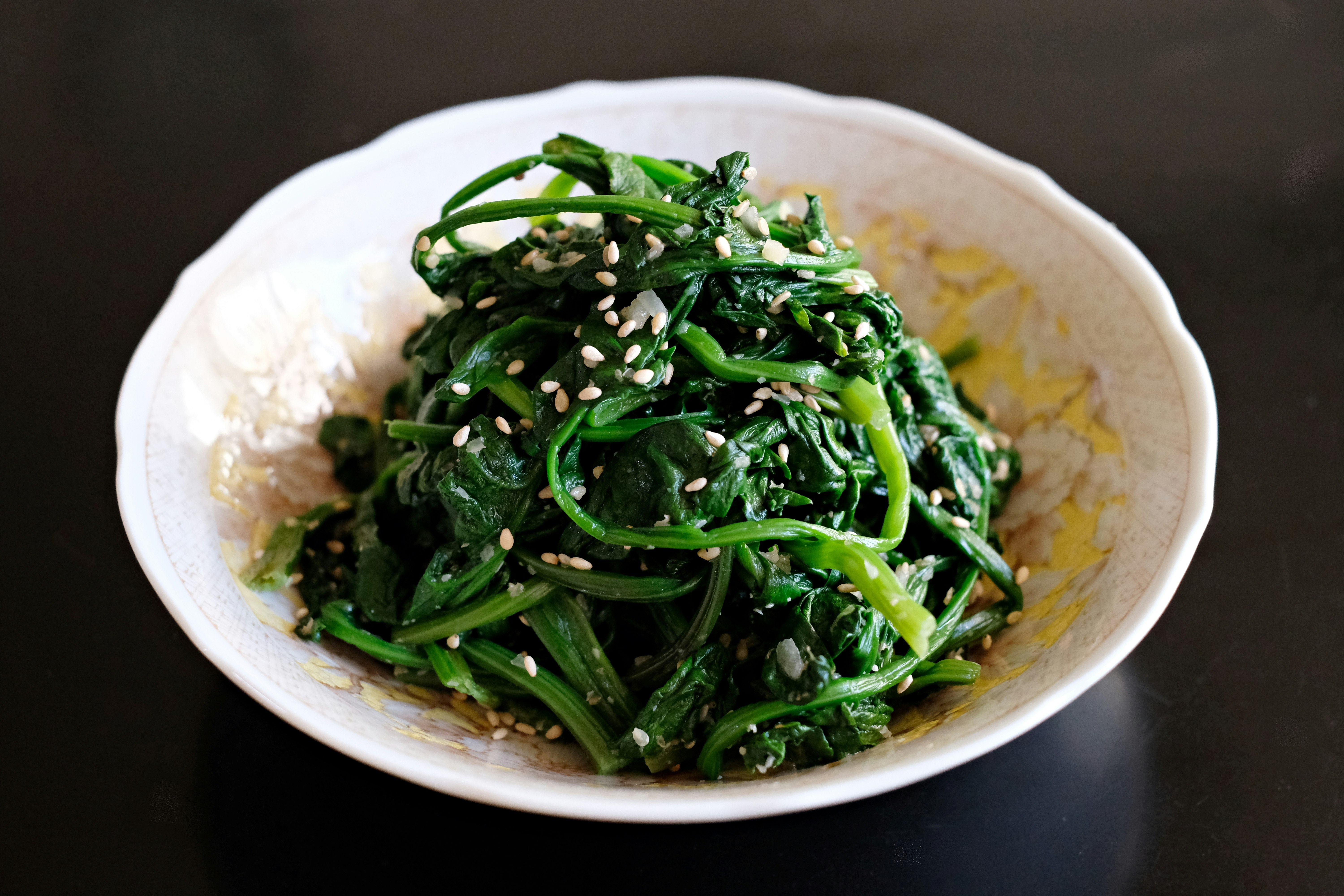 A mound of boiled and season spinach sits in a white bowl. 